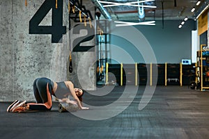 Full length of a young sportive woman in sportswear exercising with foam roller, doing stretching exercises on yoga mat