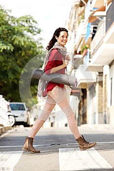 Full length young woman crossing street with yoga mat and bag