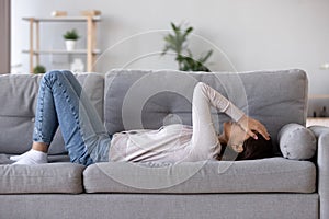 Full length young woman lying on couch suffers from heartache