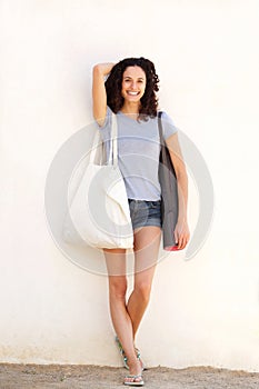 Full length young woman smiling with yoga mat and bag against white background