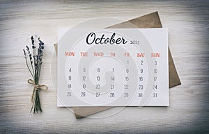 Full-month calendar: October 2021. Numbers, days of week, on white paper, on top of kraft paper envelope, next to