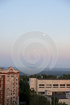 Full moon on a blue sky with pink shades of pastel colors and high-rise buildings