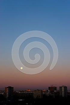 Full moon on clear sunrise sky and buildings under it