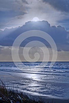 Full moon in clouds overlooking silver blue ocean water