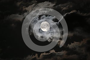 Full moon in eerie white clouds against a black ni