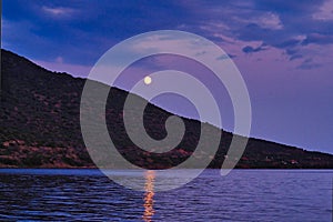 Full Moon Light Reflected in Sea Rising Over Treed Mountain Slope