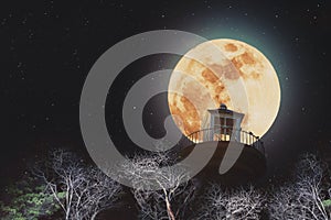 Full moon at night with lighthouse on clear sky with stars, and dead branches