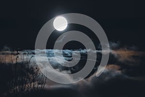 Full moon over clouds and fog in night sky, nebulous blurry landscape
