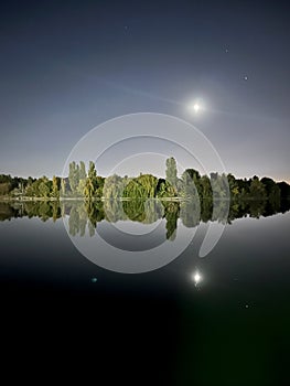 Full moon reflecting on lake with trees, landscape view