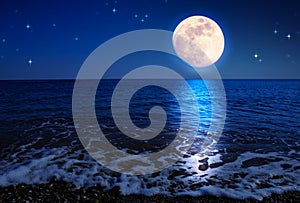 Full moon with reflections on a calm sea at midnight.