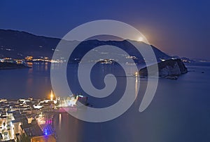 Full moon rise above Budva old city, Saint Nicholas island and Adriatic littoral, night cityscape, Montenegro, Europe. Famous photo