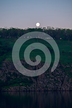 Full moon rises over the rocky banks of a large river