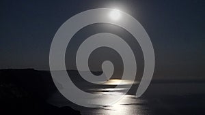 The full moon rises in a starry night sky over the sea and rocky cliffs. The concept of calmness, silence and unity with