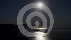 The full moon rises in a starry night sky over the sea and rocky cliffs. The concept of calmness, silence and unity with