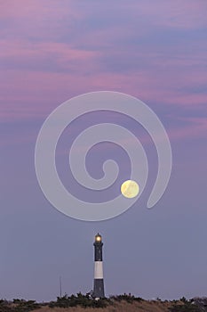 Full moon rising behind a tall stone lighthouse just after sunset. Fire Island