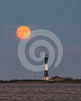 Full moon rising through a hazy horizon behind a beautiful lighthouse. Fire Island, NY