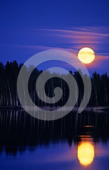 Full Moon rising over lake and forest landscape