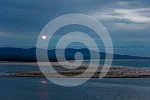 Full moon rising over lake & sea landscape at dusk