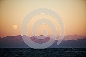 Full moon rising over sea and mountains