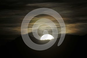 Full Moon rising with rainbow clouds in night sky