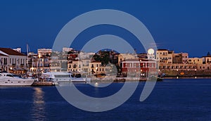 Full moon setting over Chania`s Old Venetian Harbour. Night view of piers, boats and Maritime museum of Crete and houses