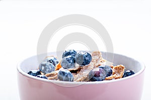 Full muesli bowl on a white table with blueberry and milk splash. Healthy breakfast cereals with milk, seed, fruit. Oat flakes