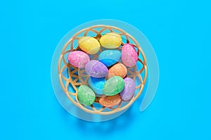 Full plastic basket of colorful eggs with glitters lies on blue table on kitchen. Easter concept. Top view