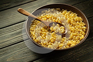 A full plate of raw pasta and a spoon on a vintage table before preparing breakfast. Place for recipe or menu on dark background