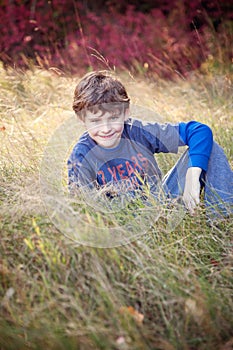 Smiling seven year old boy portrait sitting in field in Autumn
