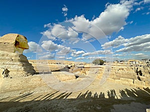 Full profile of Great Sphinx including pyramids in the background on a clear sunny, blue sky day in Giza, Cairo, Egypt with no