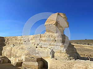 Full profile of Great Sphinx including pyramids in the background on a clear sunny, blue sky day in Giza, Cairo, Egypt with no