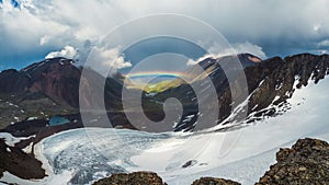 Full rainbow over a glacial mountain valley.Atmospheric alpine landscape with snowy mountains with rainbow in rainy and sunny