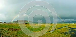 A full rainbow over rural green farmland landscape showing wet rainy weather