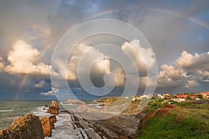 Full rainbow over sea coast with Arnia beach in Santander, Cantabria, North Spain with cliffs and flysch rocks. Popular