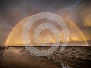 A full rainbow over the sea with storm clouds at sunset