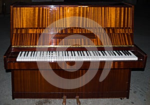 Full scale brown upright piano 88 keys keyboard. White and black keys in perspective, two pedals.
