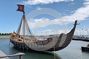 full-scale viking ship docked at harbor, with sails furled and oars in place