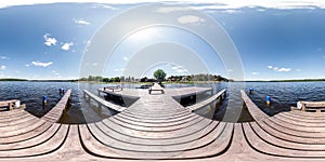 Full seamless panorama 360 by 180 angle view wooden pier for ships on huge forest lake in sunny summer day in equirectangular photo