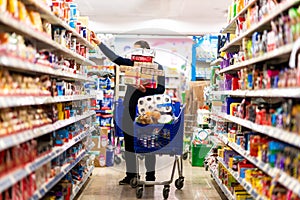 Full shopping cart, customer is stocking vital needs because of global chaos. Shopping with blur supermarket store