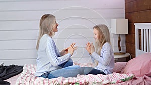 Full shot casual mother and cute baby daugher enjoying fooling clapping hands sitting on bed