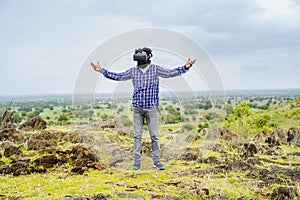 Full shot of man with VR headset feeling nature by stretching arms on top of mountain - concept of Metaverse, virtual