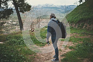 Full size dramatic shot of a hiker young man with backpack standing in the forest path and looking at the mountains