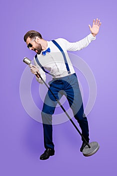 Full size fullbody portrait of famous creative singer in blue pants with suspenders, black glasses, singing hit with