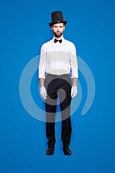 Full size fullbody portrait of stylish attractive magician in tophat, formal wear, bow, looking at camera, isolated on