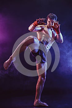 Full size of Muay thai fighter who delivering knee hit isolated on smoke background. mixed media