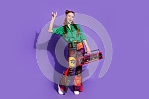 Full size photo of adorable woman dressed green shirt print trousers hold boombox show rock symbol isolated on purple