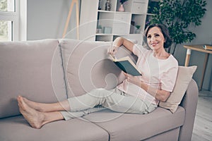 Full size photo of aged brunette nice lady sit on sofa read wear pink t-shirt trousers at home alone