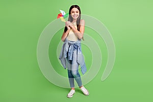 Full size photo of beautiful happy smiling good mood little girl playing with pinwheel isolated on green color