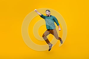 Full size photo of brave guy dressed dotted shirt brown trousers fly in empty space raising fist up  on yellow