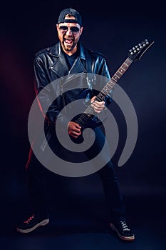 Full size photo of brutal bearded Heavy metal musician in leather jacket and sunglasses is playing electrical guitar